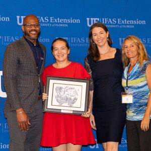 IFAS leader presents three women from the winning team with framed award.